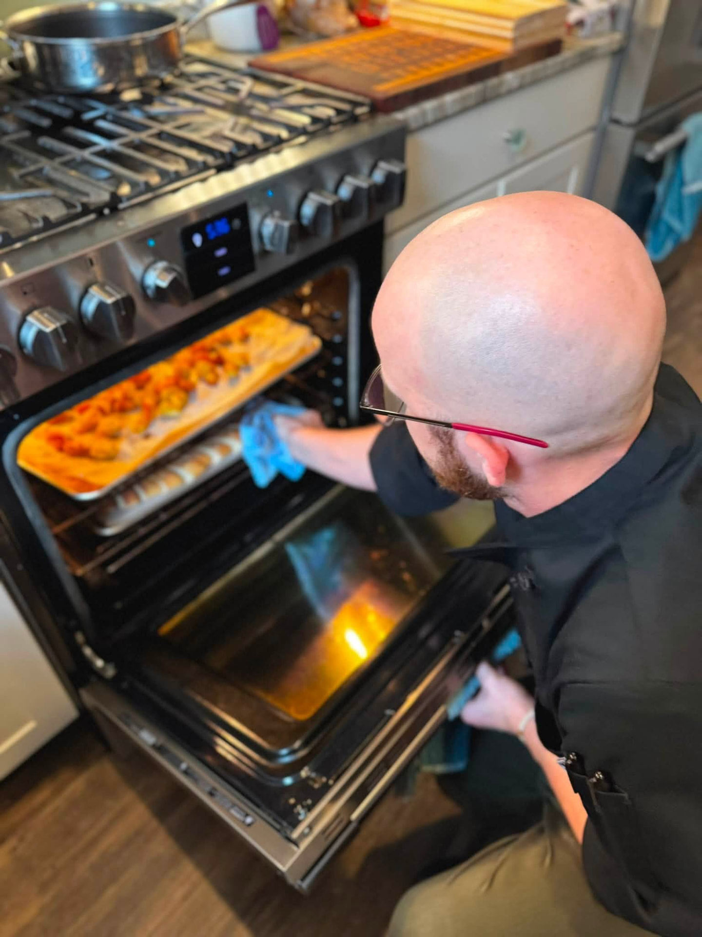 Chef Asa pulling a tray of roasted vegetables from an oven in a client's home kitchen