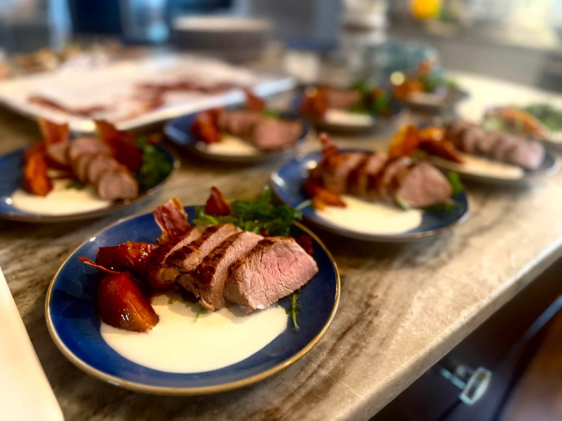 Sliced pork tenderloin with crisped prosciutto, arugula and peaches on blue plates