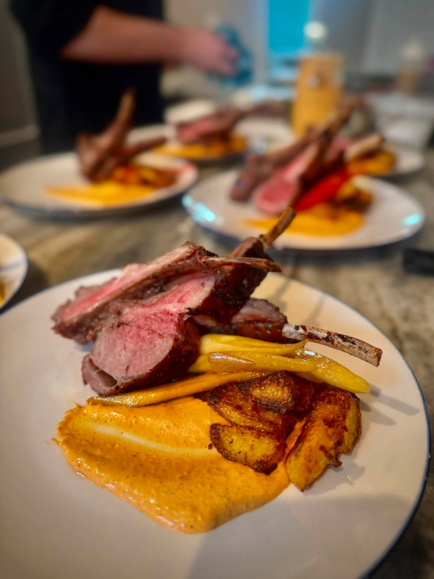 Close-up of rack of lamb lollipops with harissa cream and crispy potatoes on a white plate