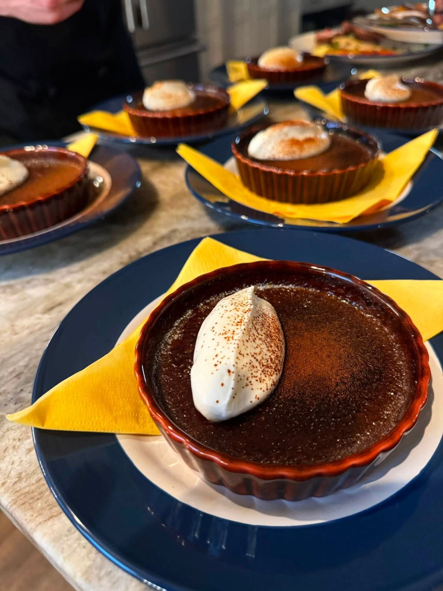 Crème brûlée in a red ramekin topped with a quenelle of cream and cocoa