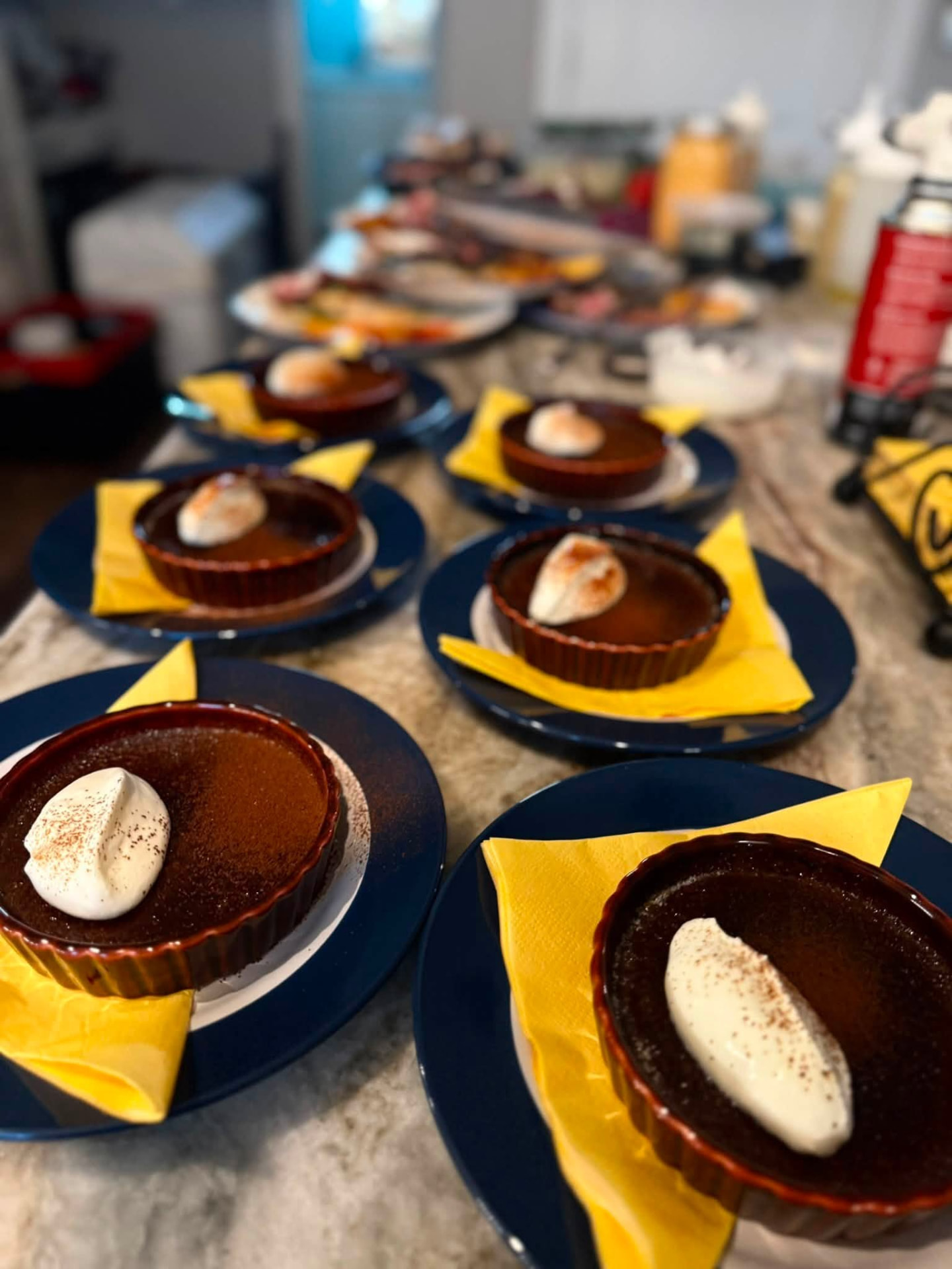 Row of crème brûlée tarts plated on blue dishes with yellow napkins