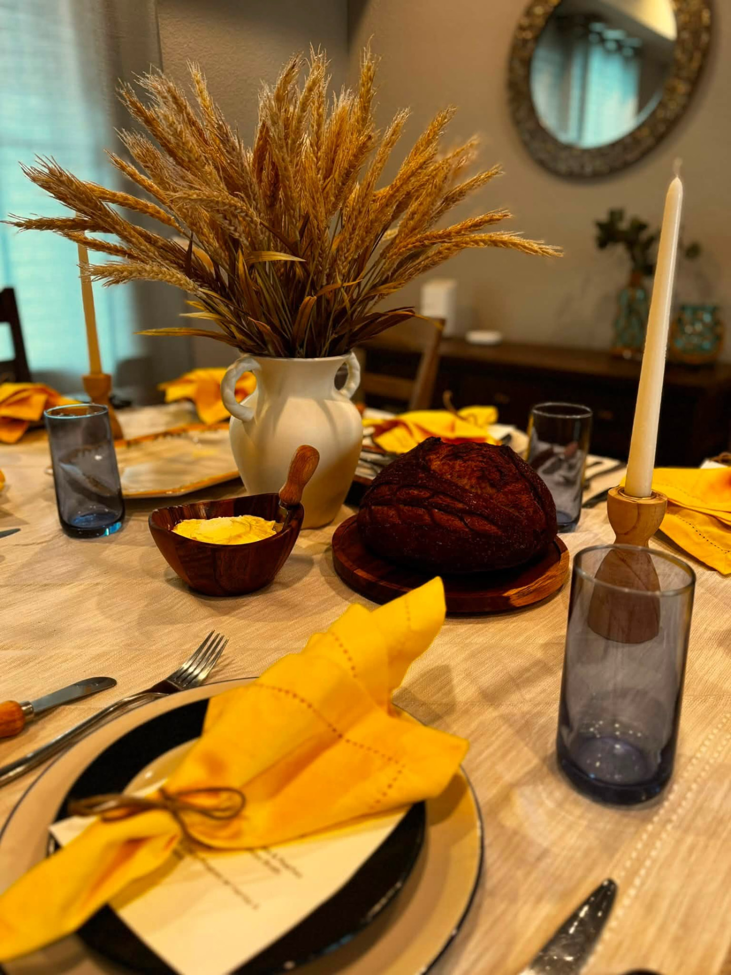 Dinner table set with yellow linen napkins, candles, house bread and butter