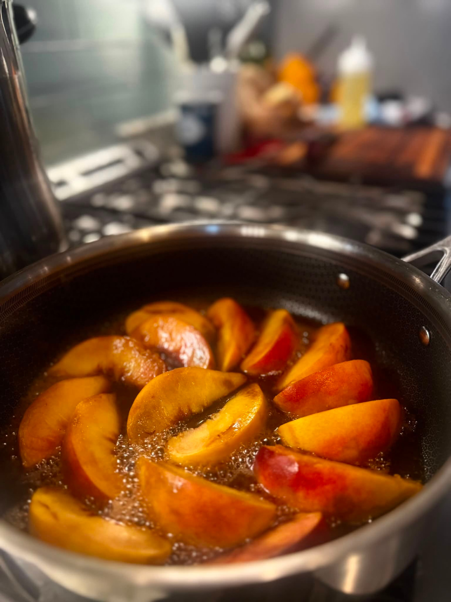 Sliced peaches simmering in a spiced caramel syrup in a stainless pan on the stove